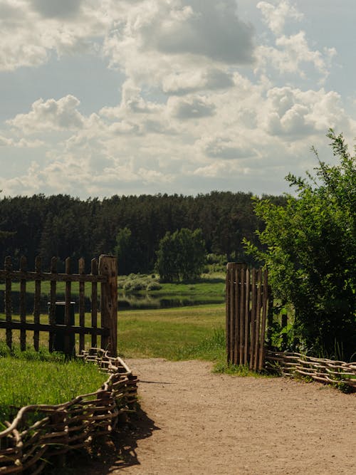 Brown Wooden Fence Across the Green Grass Field Under White Clouds