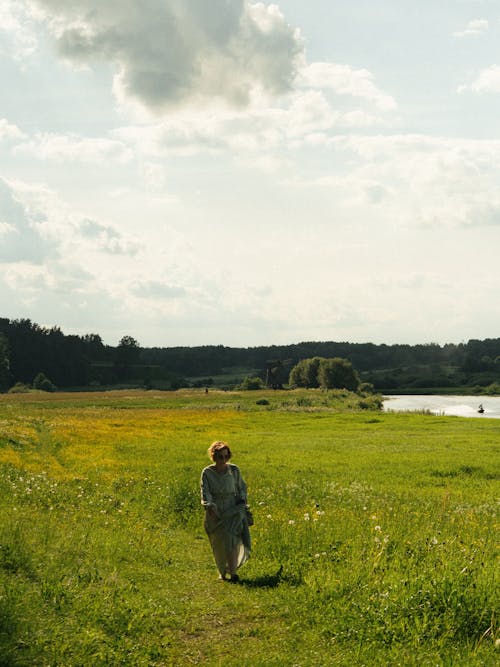 A Woman in Long Dress Walking on Green Grass Field