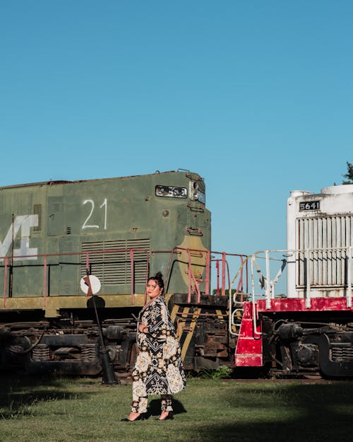 A Woman in Printed Dress Standing Near the Train Under the Blue Sky