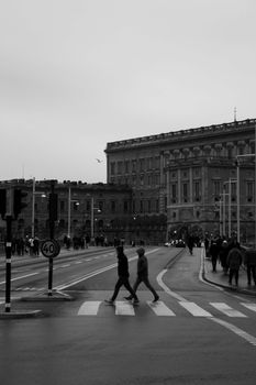 Silhouettes crossing a city street with historic buildings in black and white.