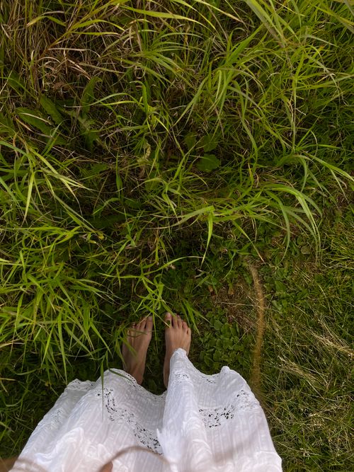 Free A serene top view of a woman standing barefoot on lush green grass in a white dress. Stock Photo