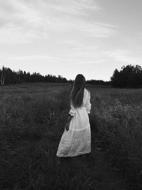A Grayscale Photo of a Woman in White Dress Standing on Grass Field