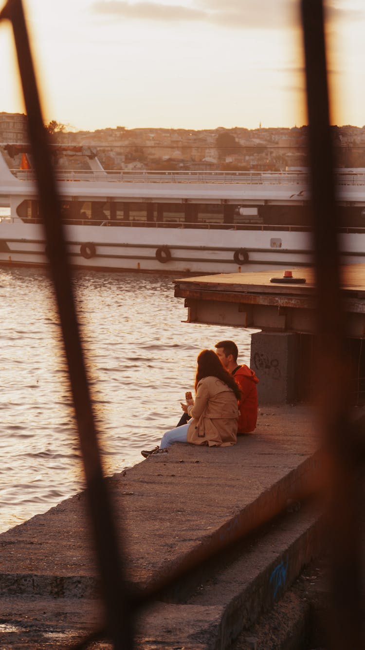 Couple Sitting On A Dock Near A Ferryboat