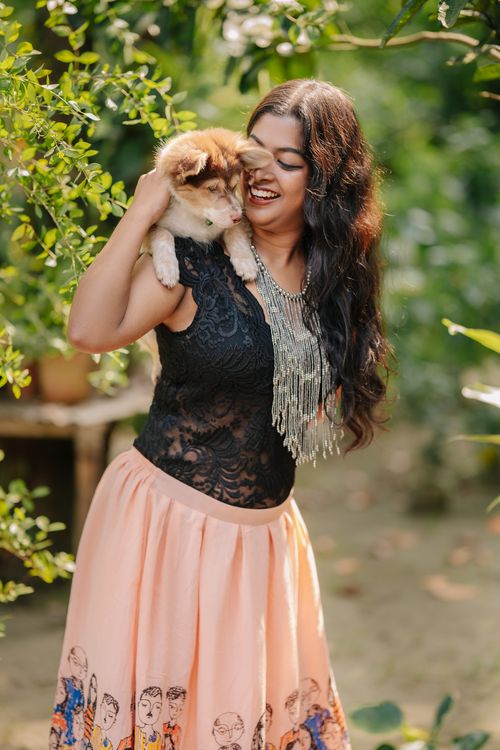 Free Smiling woman in a garden holding a fluffy puppy on her shoulder, adorned with a statement necklace. Stock Photo