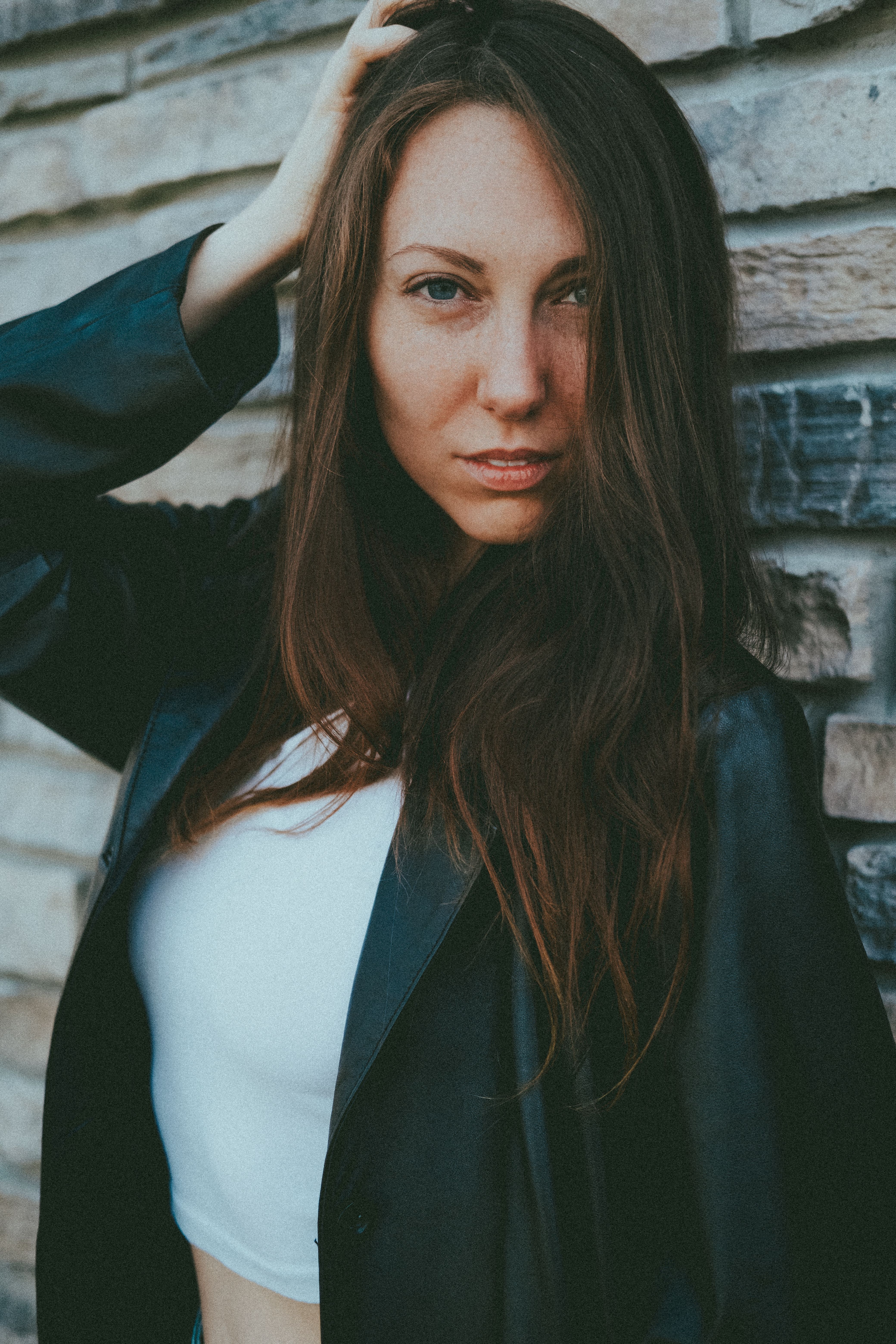 Portrait of a brunette woman in casual attire, posing confidently against a textured wall.