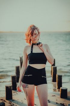 Portrait of a fashionable woman standing confidently near the ocean at sunset.