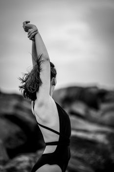 Artistic black and white photo of a woman in a swimsuit stretching against a natural backdrop.