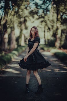 Woman posing in a black dress and boots on a tranquil tree-lined path.