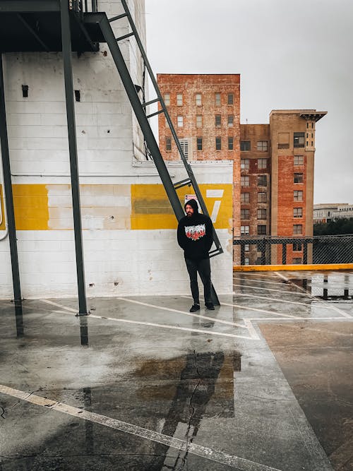Man in Black Hoodie and Black Pants Standing on Rooftop with Wet Ground