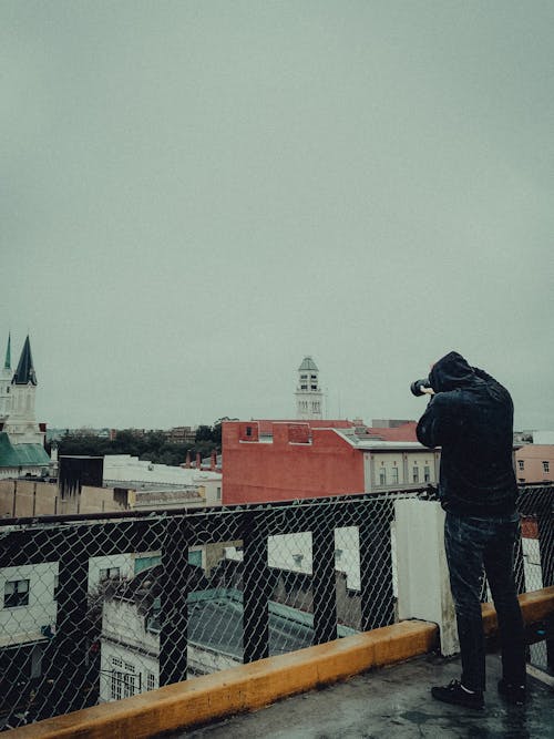 Man in Black Jacket Taking Photo from Roof Top