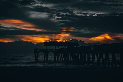 Silhouetted pier against a dramatic sunset sky over the ocean, creating a scenic and tranquil view.