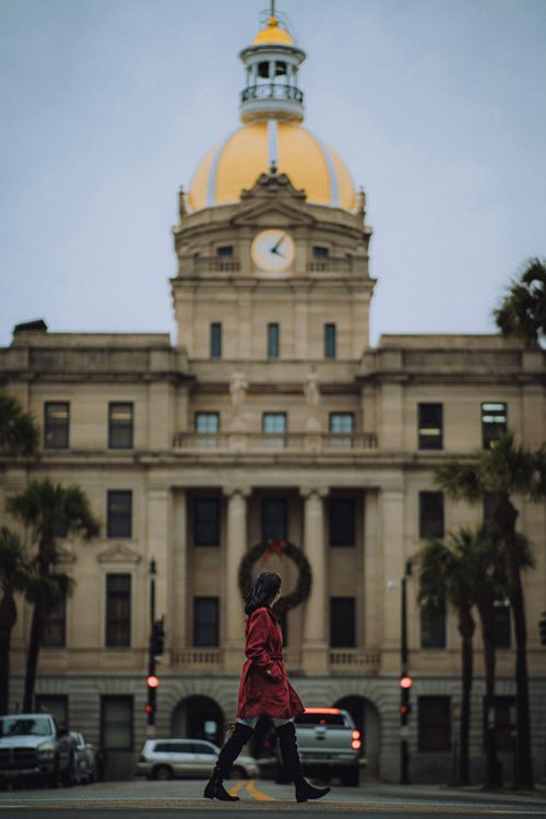 Free A woman in a red coat walks past the iconic Savannah City Hall with a golden dome. Stock Photo