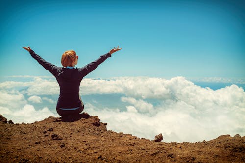 Free Person Sitting on Cliff Raising Up Both Hands Stock Photo