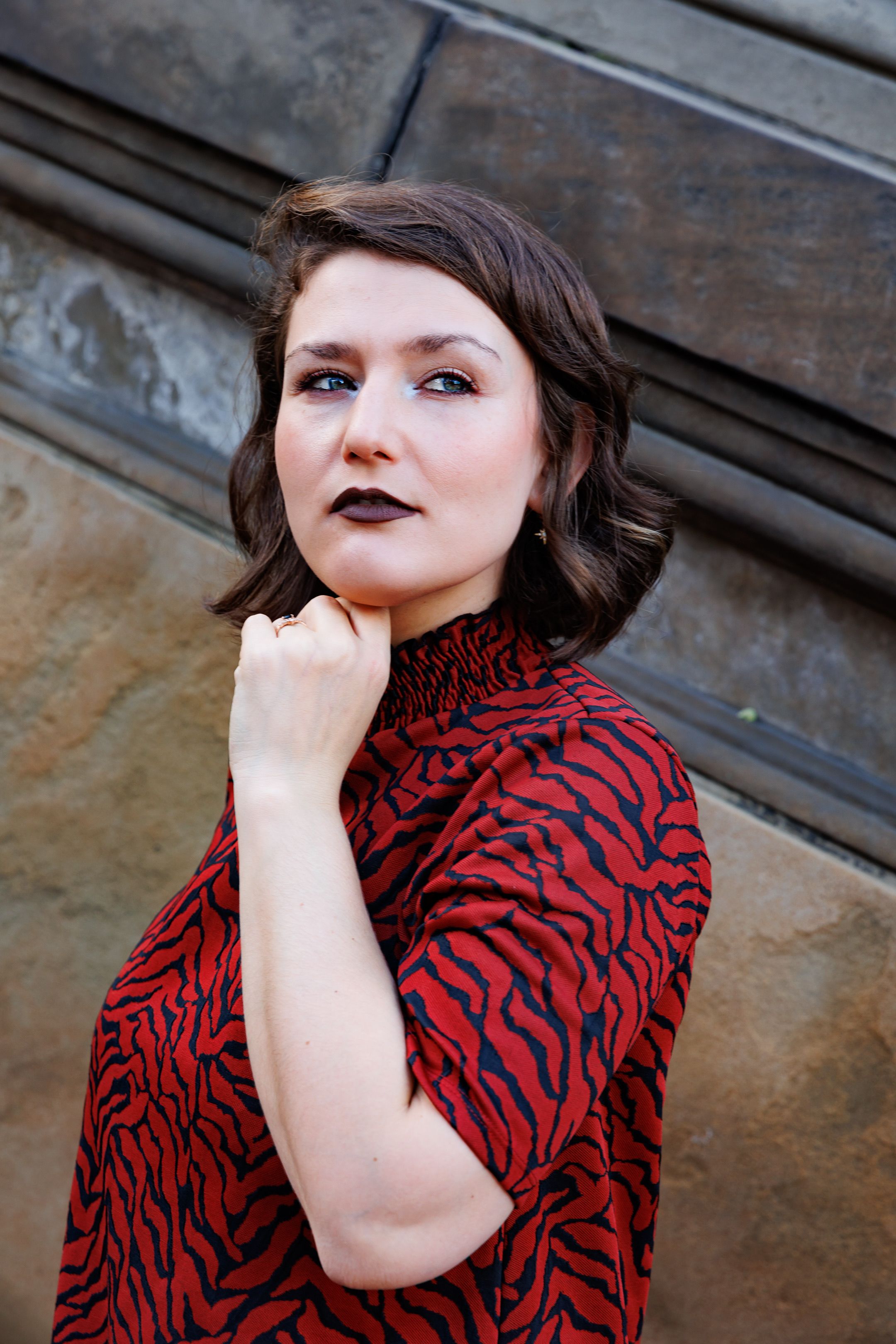 Portrait of a woman with brown hair and vibrant red outfit, thoughtfully posing outdoors.