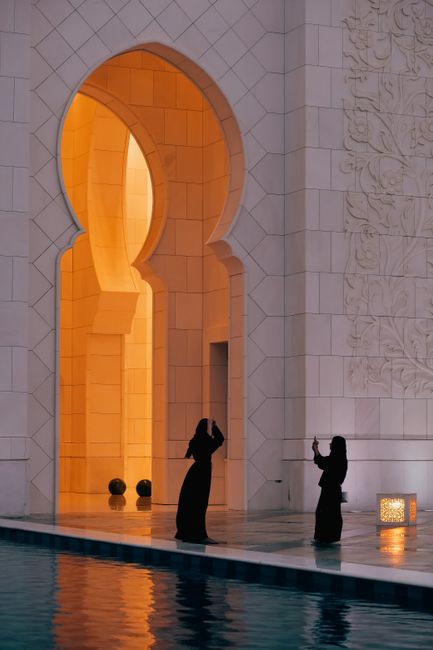 Two women in traditional attire by a pool in an ornately designed building, capturing a moment.