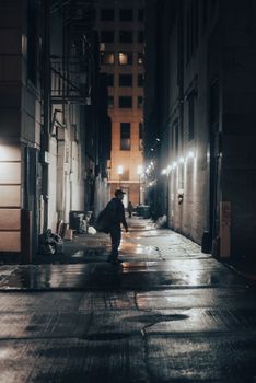 A solitary figure walks through an illuminated alley at night, creating a dramatic urban ambiance.