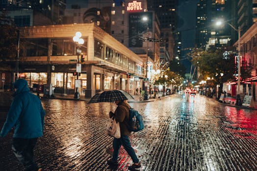 A person with an umbrella walking in a vibrant, rainy downtown street at night, surrounded by urban lights.