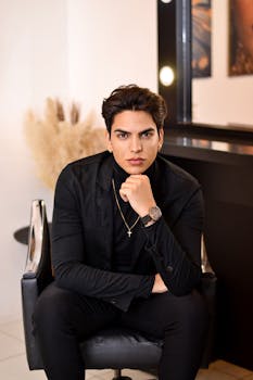 A fashionable man poses confidently in a salon chair, exuding modern style.