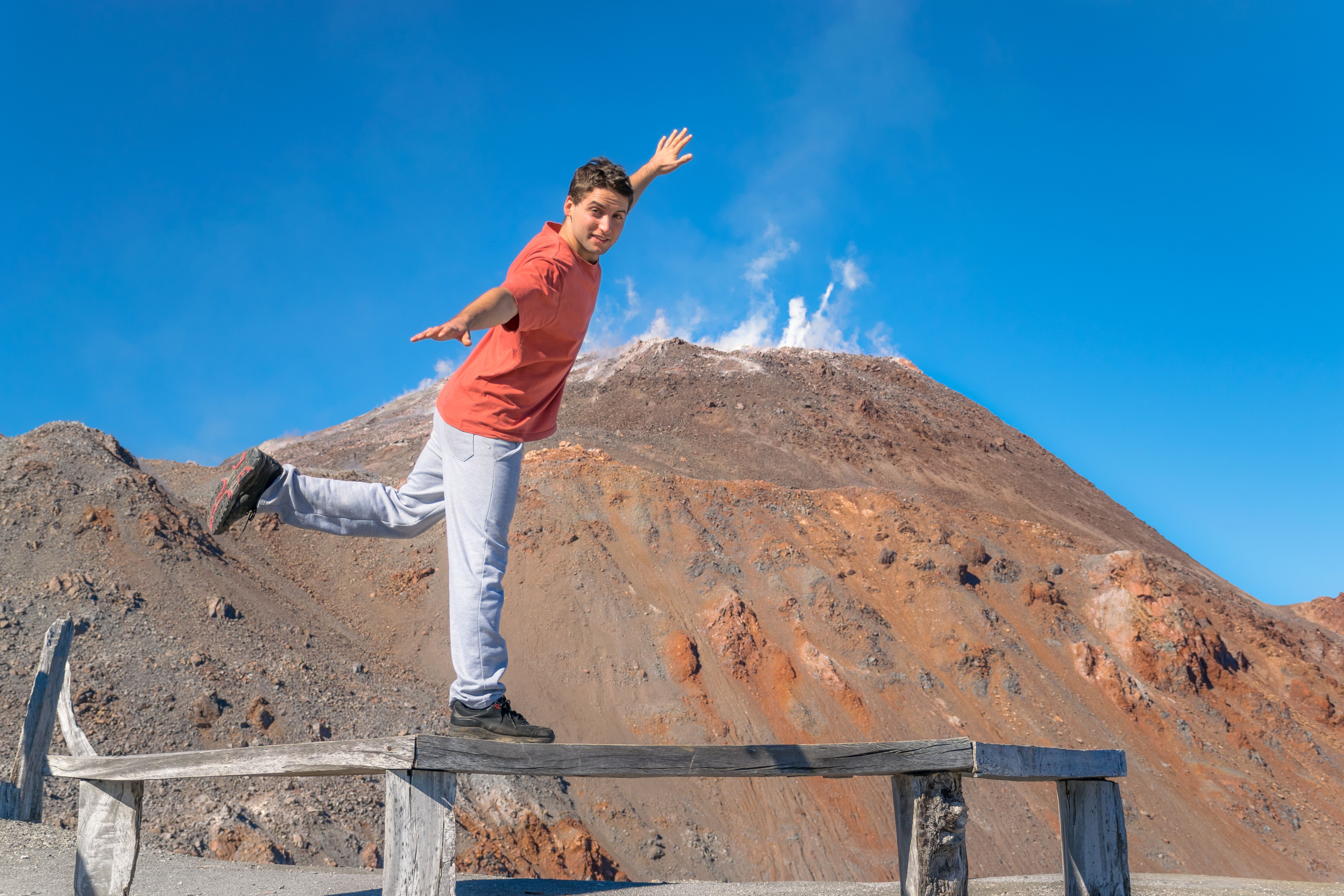 Man balancing on wooden beam with volcano in background, Chaiten, Chile.
