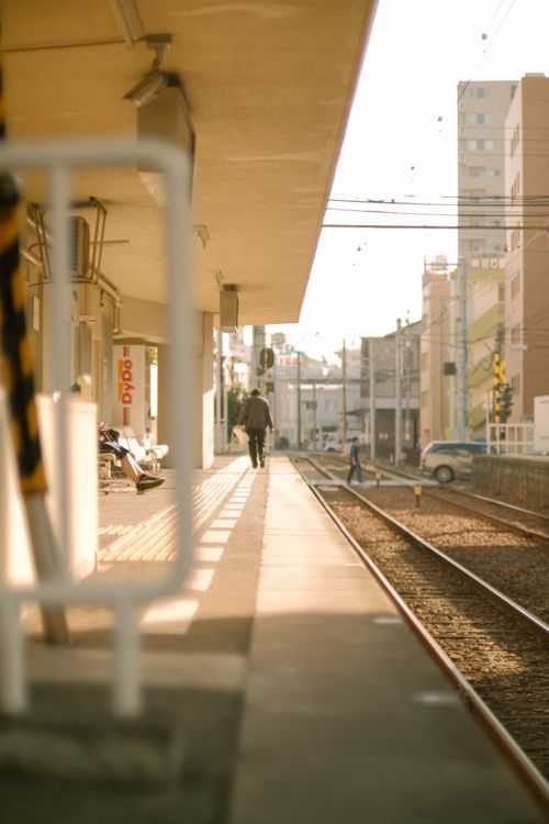Free Urban railway station platform with warm sunlight and people walking along the tracks. Stock Photo