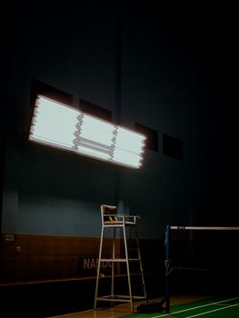 Dimly lit indoor sports hall featuring a volleyball net and bright overhead lighting.