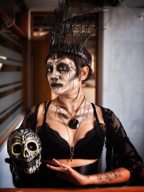 Free Woman in eerie witch costume holding skull, performing a dark ritual indoors, perfect for Halloween themes. Stock Photo