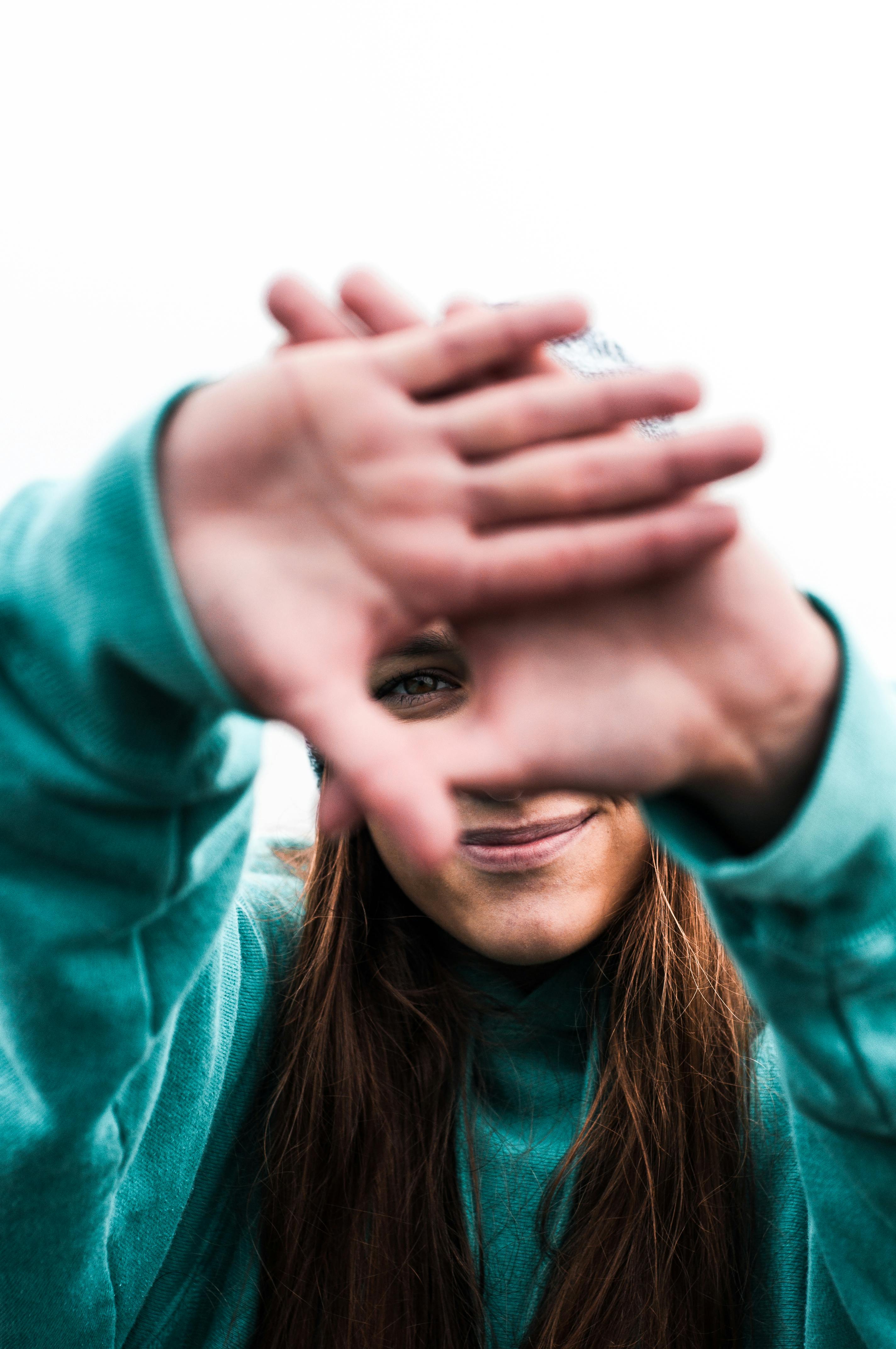 Cheerful young woman playfully framing her face with hands outdoors.