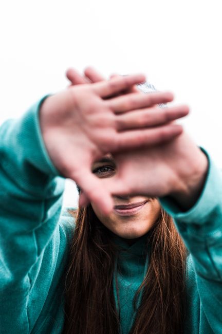 Cheerful young woman playfully framing her face with hands outdoors.