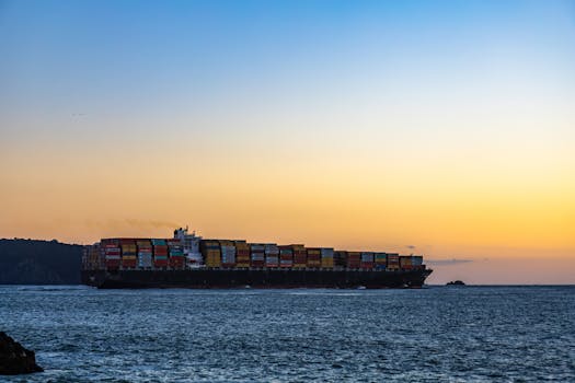 A massive cargo ship sails across the ocean against a vibrant sunset sky.