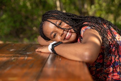 Free Cheerful woman with braided hairstyle enjoys a sunny day outdoors, resting on a wooden table. Stock Photo