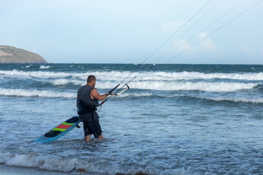 Adult man preparing to kiteboard in the ocean waves, enjoying a sunny beach day with his surfboard.