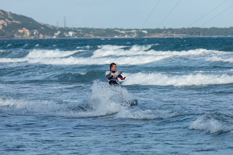 A Man In White Wet Suit Surfing On Sea Waves With A Kite Board