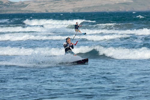 A Man in White Wet Suit Surfing on Sea Waves with a Kite Board