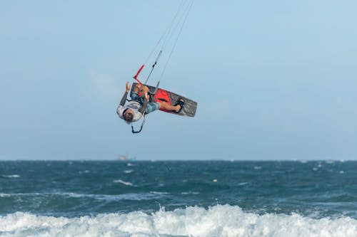 A Man Wearing a White Shirt on Air Riding a Kite Board Over Wavy Body of Water