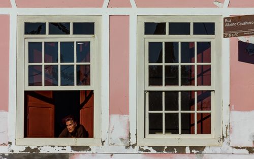 Free A person looking out from a vintage window in a sunlit pink wall. Stock Photo