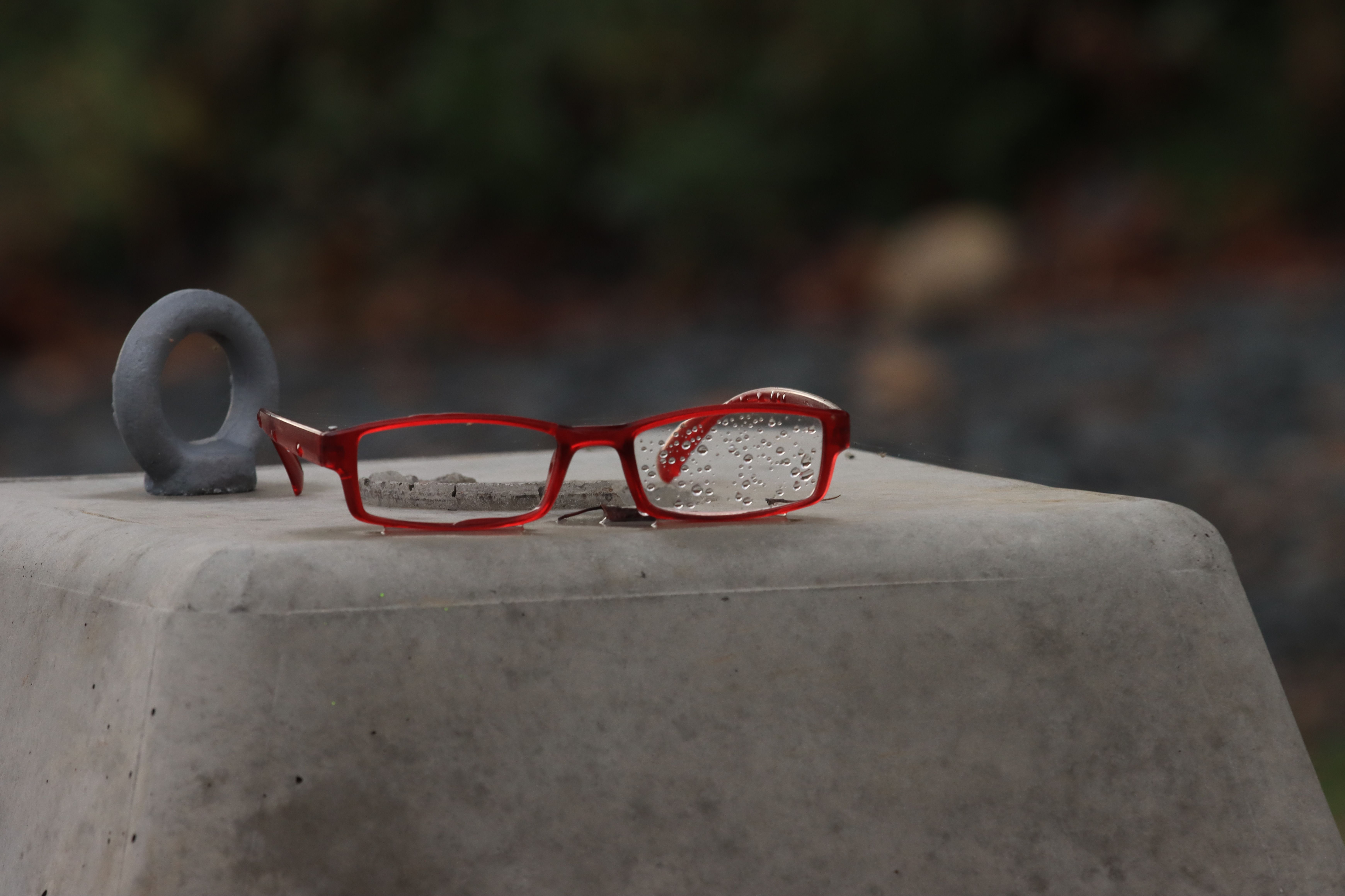 Red eyeglasses with raindrops on a concrete surface outdoors. Capturing serenity.