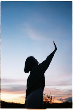 A woman silhouetted against a colorful sunset in Dalat, Vietnam, raising her arm.