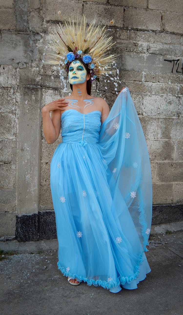 A Woman With A Face Paint Wearing A Blue Dress And A Headdress