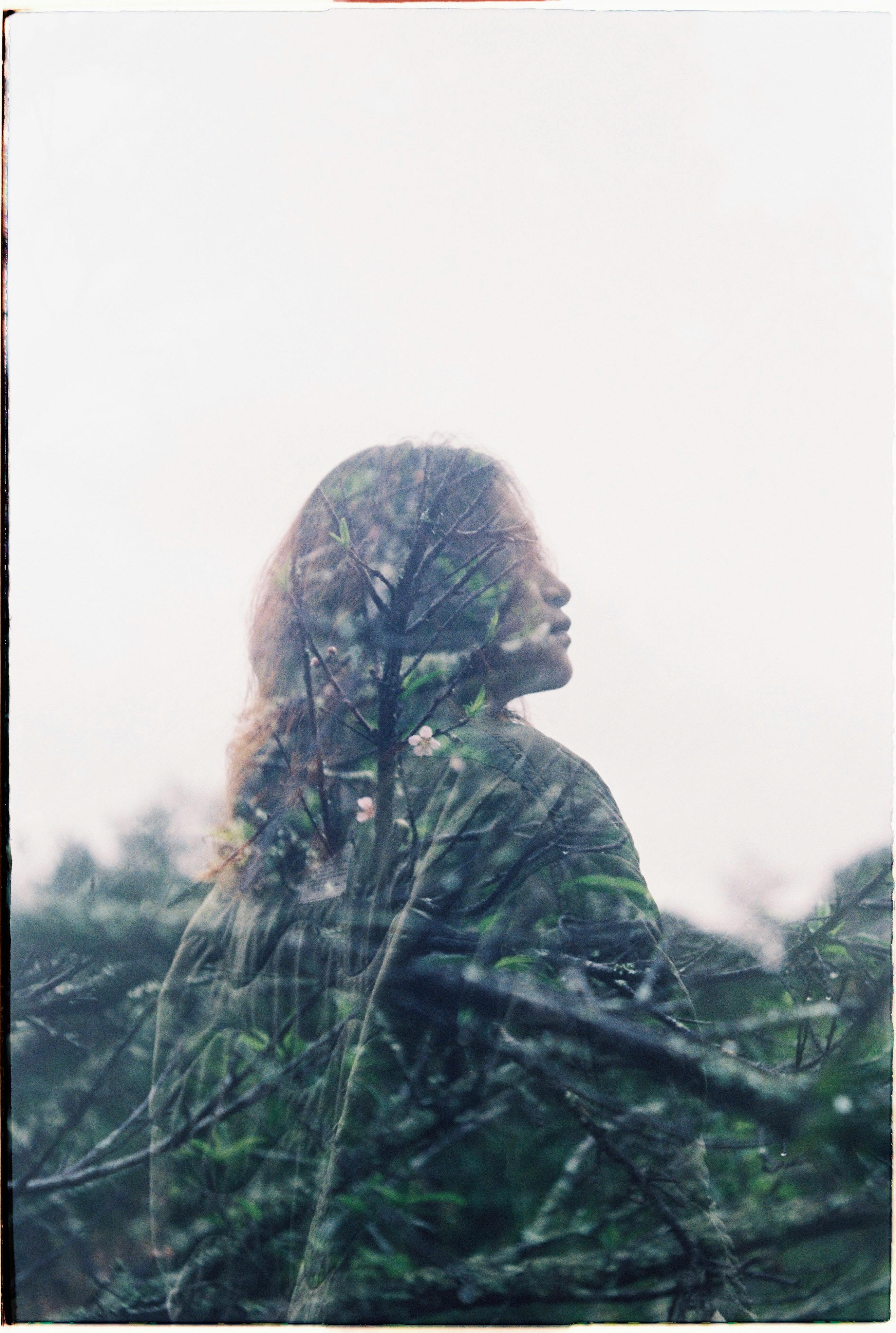 A creative double exposure shot combining a woman's silhouette with lush tree branches.