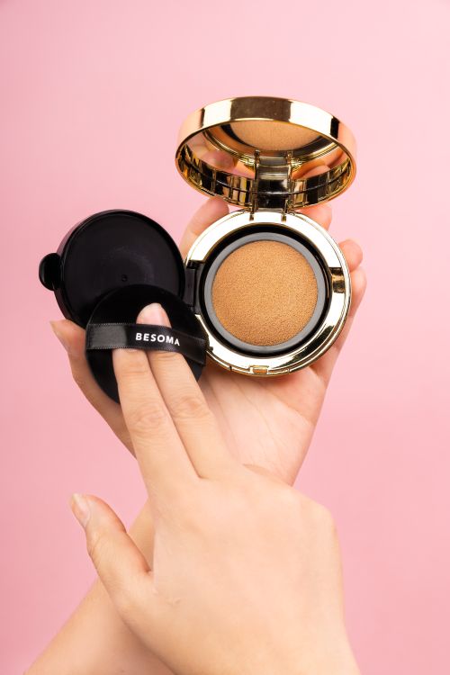 Free Hands applying makeup with golden compact on a pink background. Stock Photo
