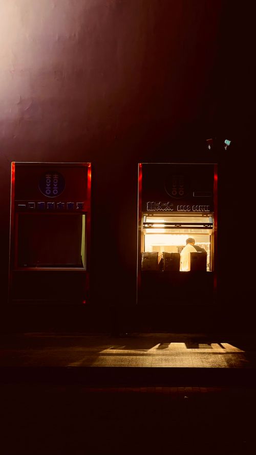 Free Atmospheric night scene of a shop with a man inside, illuminated by warm light. Stock Photo