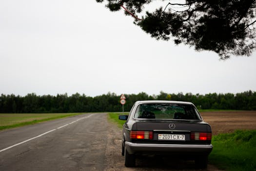 A vintage Mercedes Benz parked by a serene countryside road, perfect for travel and exploration themes.
