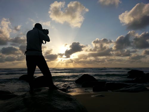 Orang Yang Mengambil Foto Di Dekat Laut Di Bawah Langit Biru Dan Putih Berawan Pada Siang Hari