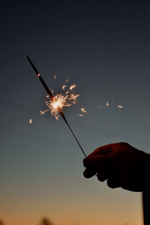 Person Holding Sparkler on Sunset Sky