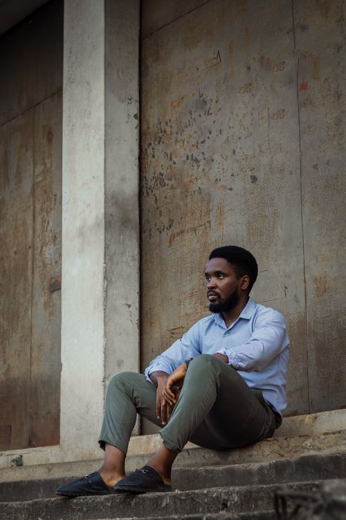 Free Black man sitting against an urban wall in Ogun State, Nigeria. Stock Photo