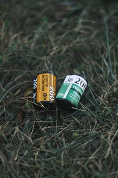 Two vintage 35mm film rolls lying on grass, evoking nostalgia and classic photography.