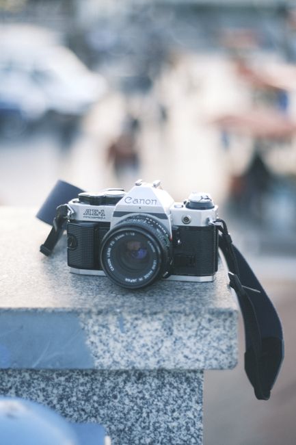 Close-up of a vintage Canon camera on a ledge with a blurred, bustling background.