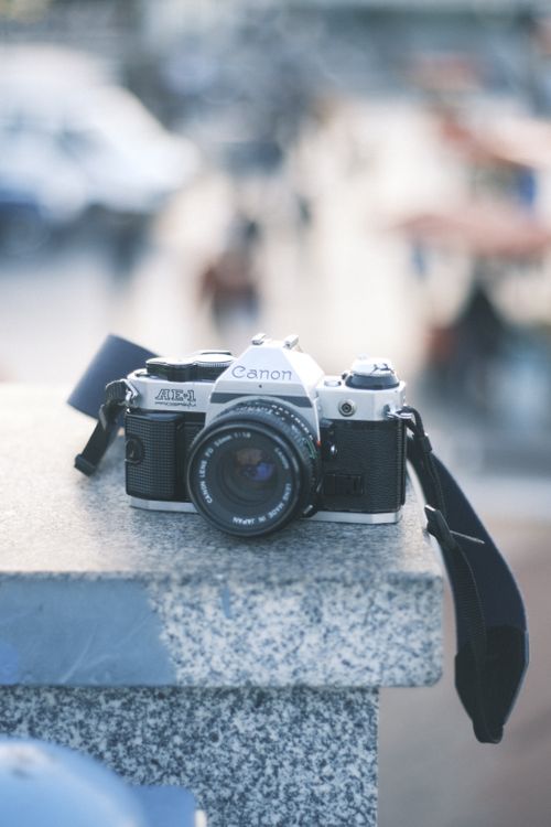 Free Close-up of a vintage Canon camera on a ledge with a blurred, bustling background. Stock Photo