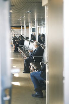 Passengers seated and waiting at a modern ferry terminal, engaged in their devices.