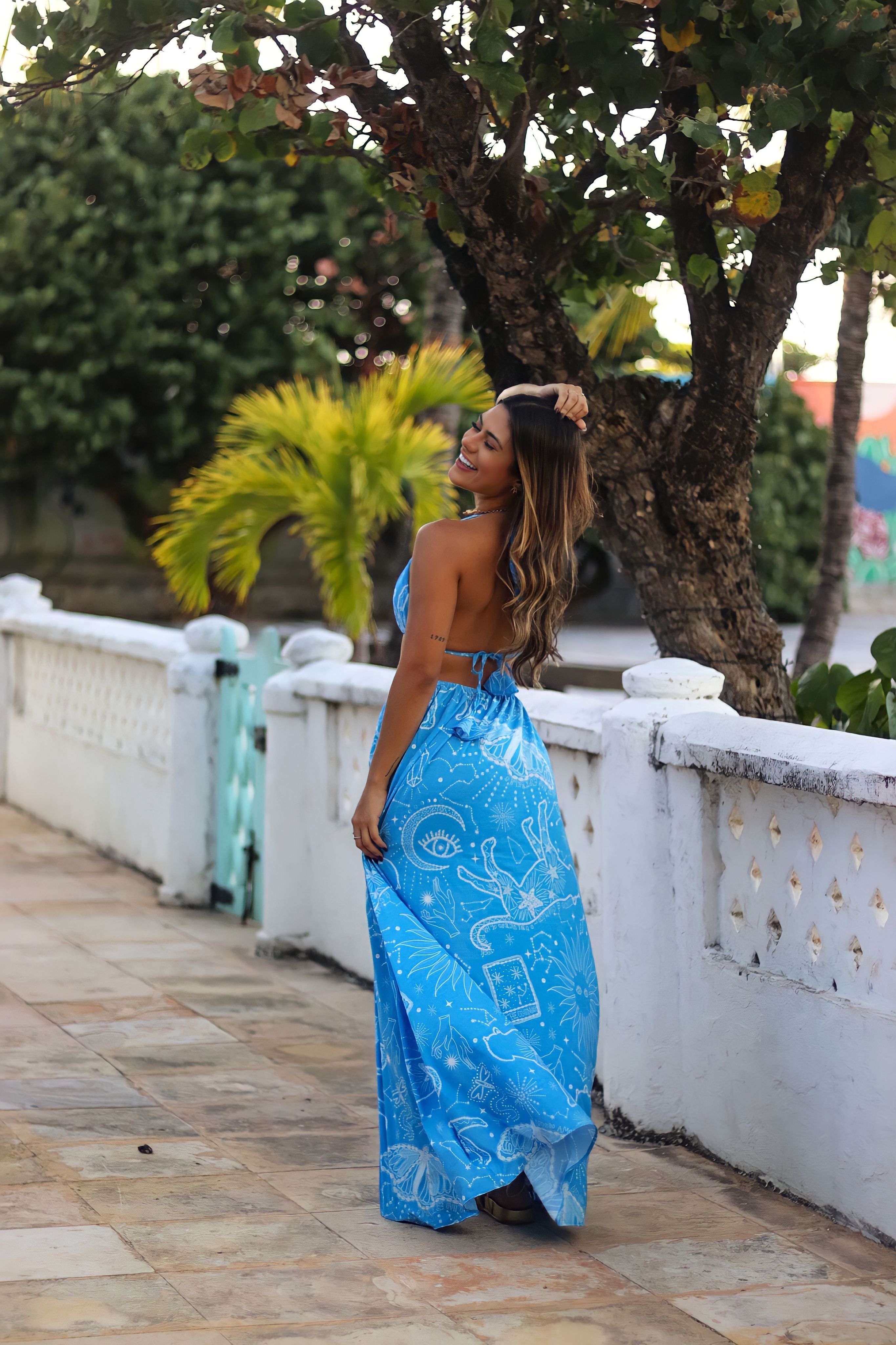 Smiling woman wearing a blue dress in a tropical outdoor setting